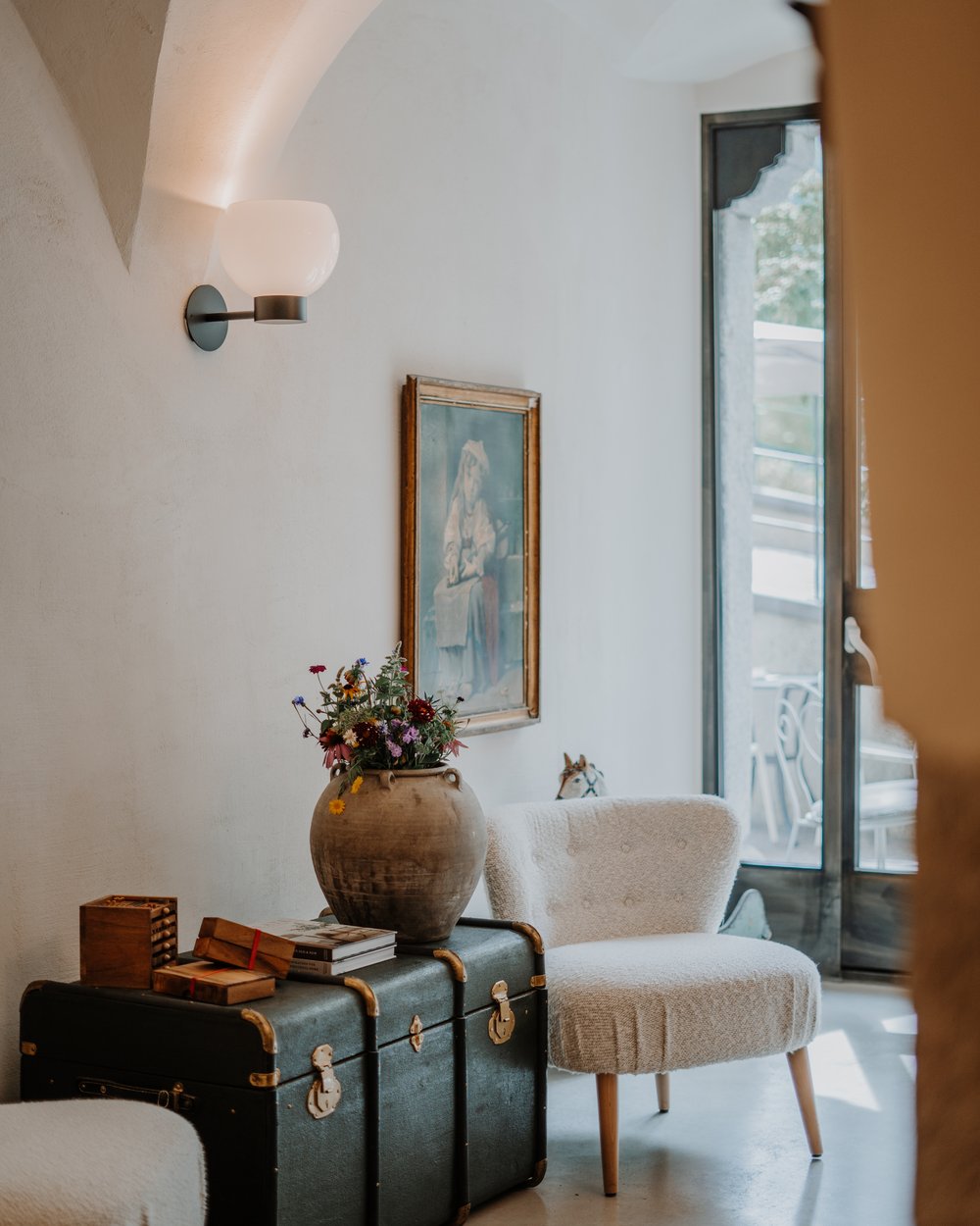 Gemütliche Sitzecke mit Sessel, antikem Koffer und Blumenvase in hellem Raum