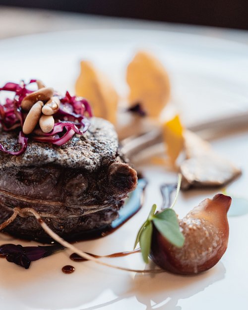 Gourmet-Steak mit Pinienkernen und Rotkohl auf weißem Teller kunstvoll angerichtet
