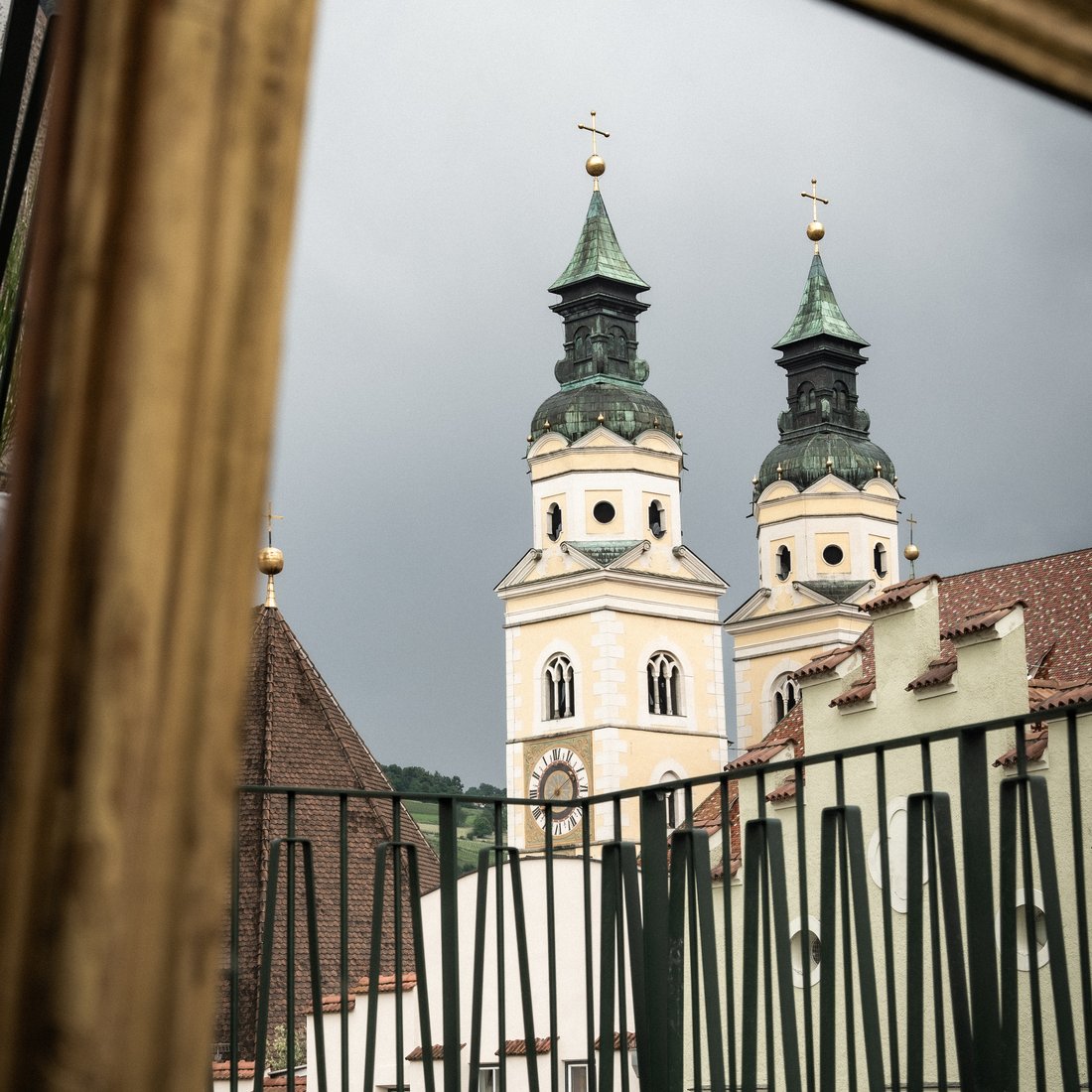 Kirchturm mit zwei Spitzen und Uhr hinter einem goldenen Bilderrahmen