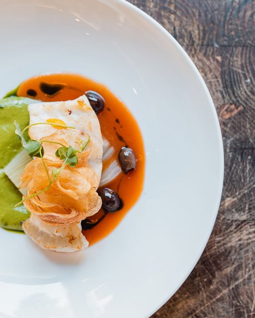 Kunstvoll angerichtetes Fischgericht mit grüner und roter Sauce auf weißem Teller