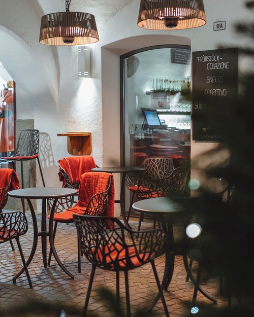 Leerer Außenbereich eines Cafés mit Tischen, Stühlen und roten Decken unter Lampen