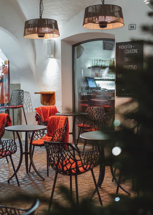 Leerer Außenbereich eines Cafés mit Tischen, Stühlen und roten Decken unter Lampen