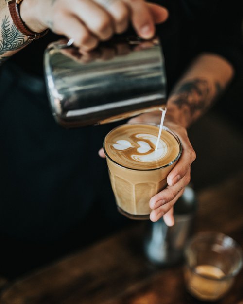 Barista gießt Milch in Kaffee mit Herz-Latte-Art auf dem Schaum