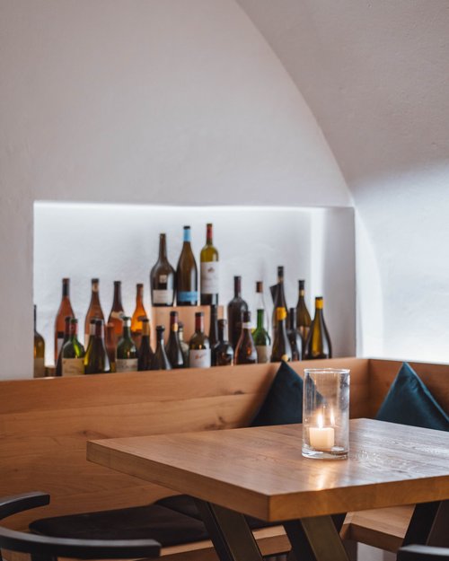 Gemütliche Sitznische mit Kerze und vielen Weinflaschen im Hintergrund