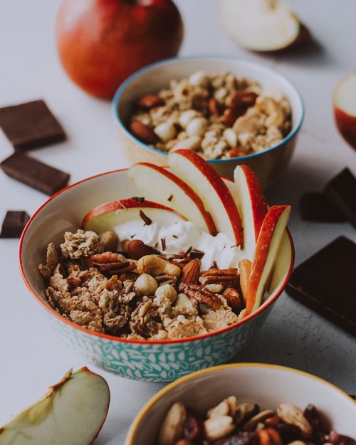 Schüssel mit Müsli, Nüssen, Apfelscheiben und Joghurt