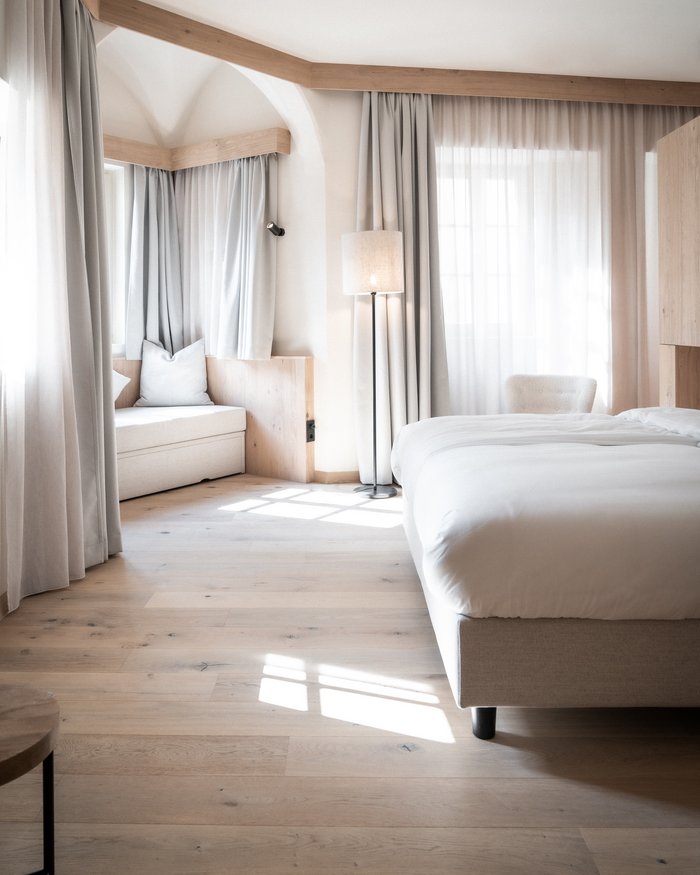 Helles Schlafzimmer mit Holzfußboden, Bett, Sitzbank und Vorhängen
