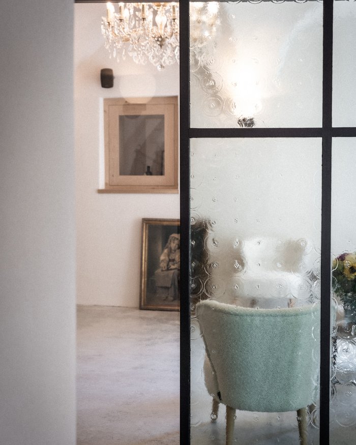 Blick durch eine raue Glastür auf einen hellen Raum mit Stuhl und Kronleuchter