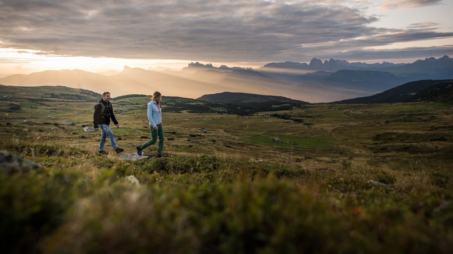 Two hikers walking in the mountains at sunset