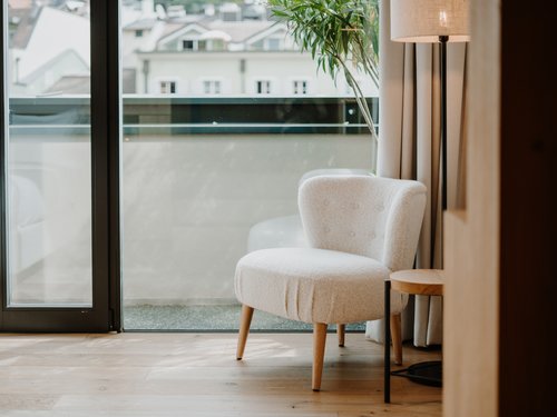 Heller Sessel neben Stehlampe und großem Fenster mit Blick auf Gebäude